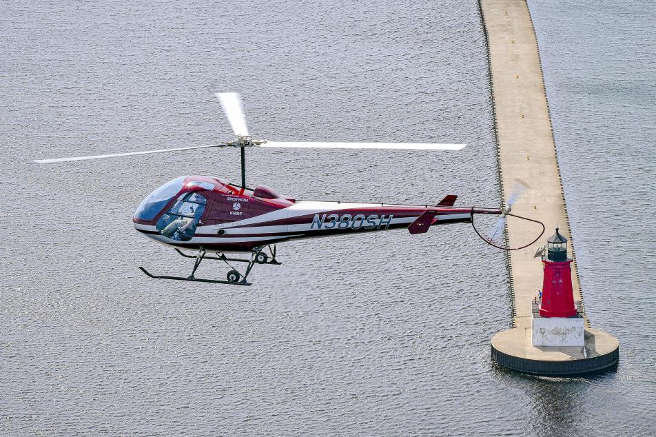 Helicopter soaring above a serene water scene with a picturesque pier and a charming lighthouse.