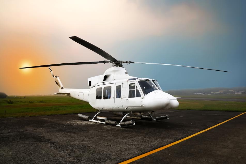 A helicopter parked on a runway with a breathtaking sunset in the background. The vibrant colors of the setting sun create a picturesque scene, enhancing the beauty of the aircraft.