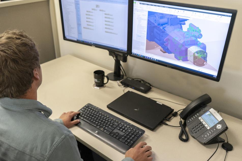 An employee immersed in their work at a computer workstation, utilizing Model-Based Systems Engineering (MBSE) methodologies to intricately design a project. 